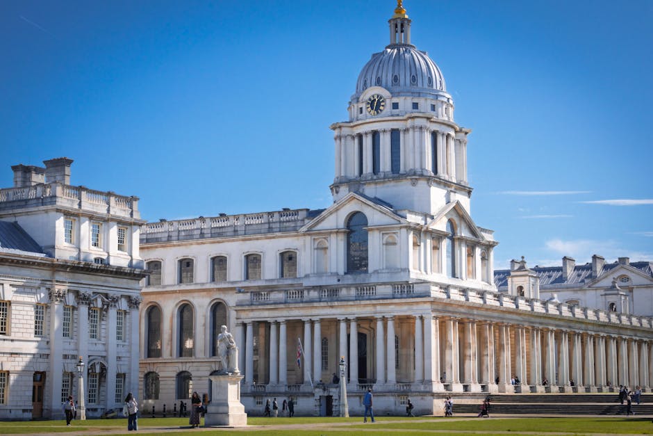 The image showcases a historic building with classical architecture, featuring a prominent dome topped with a golden finial and ornamental details. In the foreground, there is an open grassy area surr